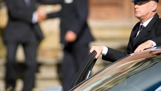 Chauffeur opening a car door for an official meeting outside a formal residence, illustrating PEP screening context in the UAE